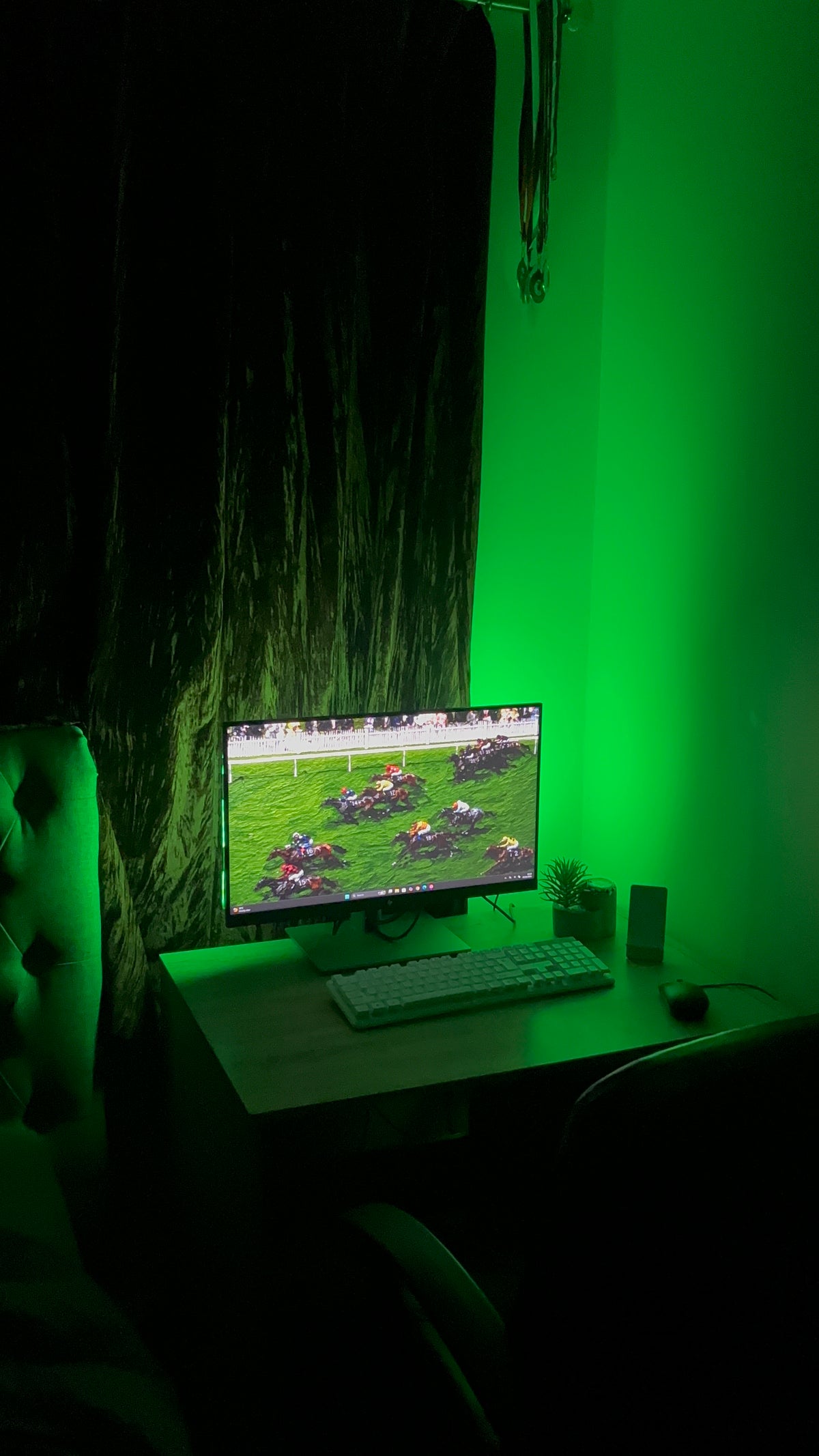 A monitor on a desk in a dark room showing horse racing, with the wall behind it lit the same bright green.